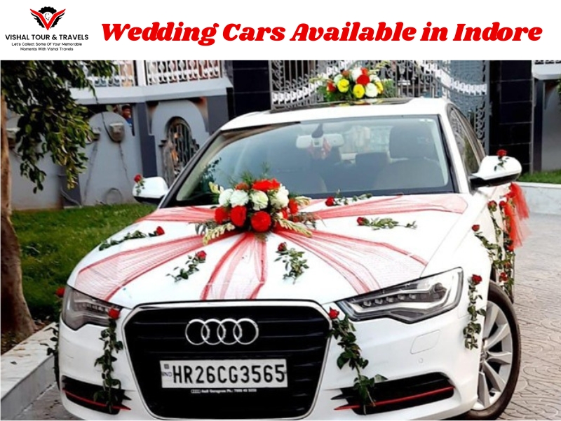 A white Audi sedan decorated with flowers and ribbons, parked outside a building, promoting wedding car rental services available in Indore by Vishal Tour & Travels.