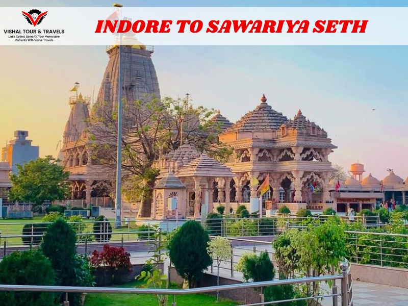 Front view of the beautifully lit Sawariya Seth temple complex with gardens in the foreground and the text “Indore to Sawariya Seth” on a travel banner.